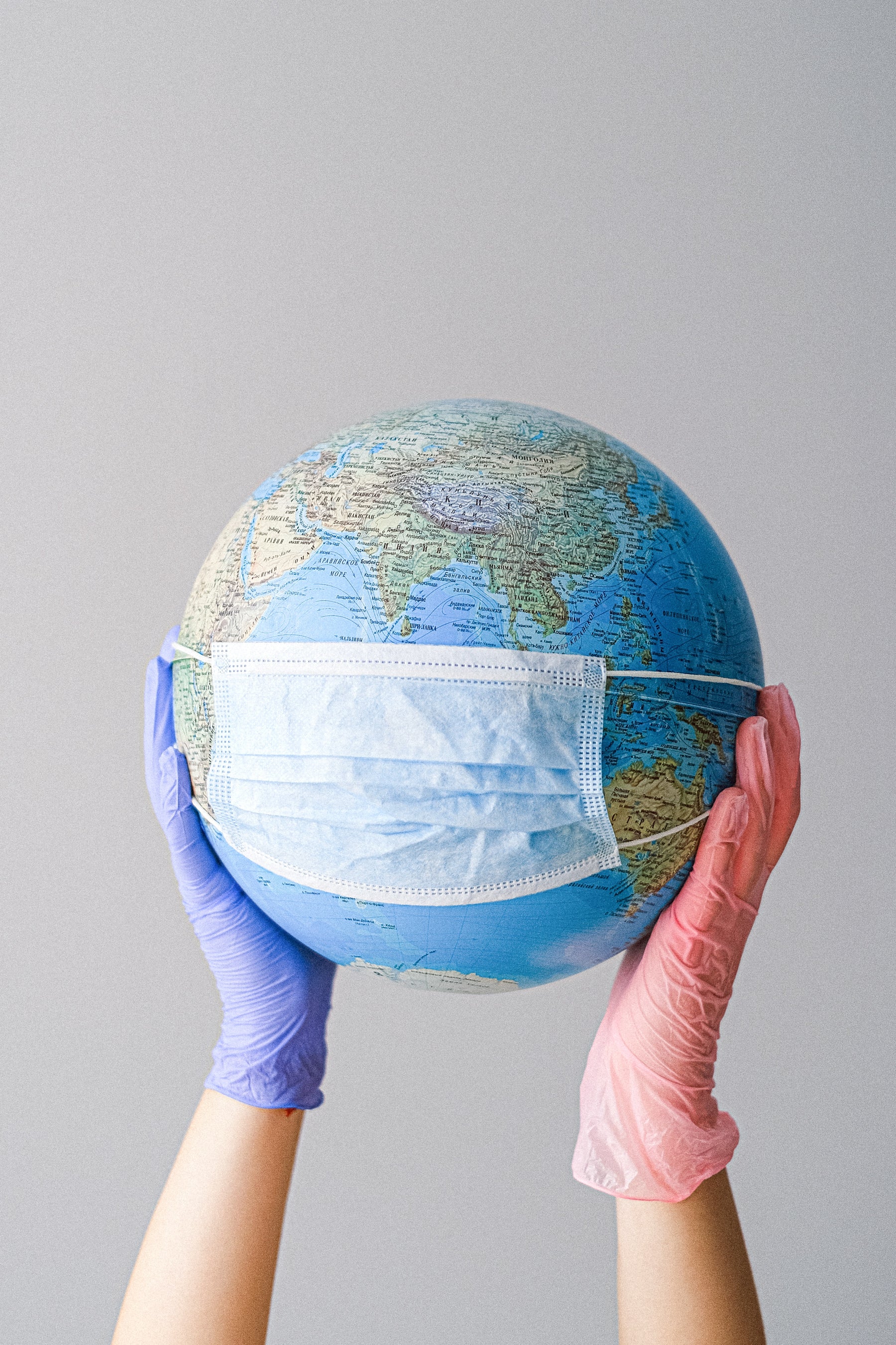 A person with gloved hands holding a globe with a mask 